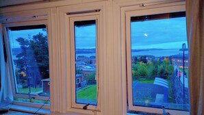 Una habitación con tres ventanas amplias que ofrecen vistas a un paisaje urbano y una masa de agua.
