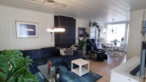 Una sala de estar moderna con un sofá seccional, una mesa de centro y un mueble para televisor. Se observa un comedor con una mesa y sillas al fondo.