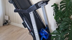 Una bicicleta estática con un portavasos azul, un enchufe y un cuadro en la pared.
