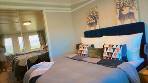 Un dormitorio con una cama grande, dos mesitas de noche, una ventana con cortinas y un cuadro con un árbol y ciervos.