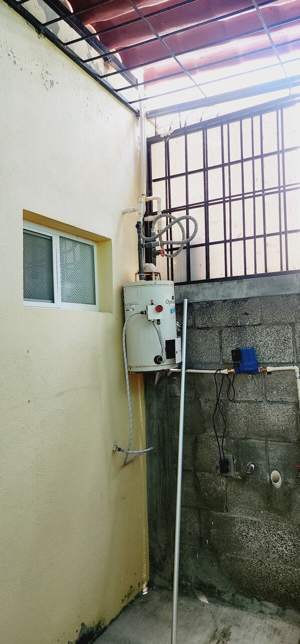 A utility room with a water heater, pipes, and a window.