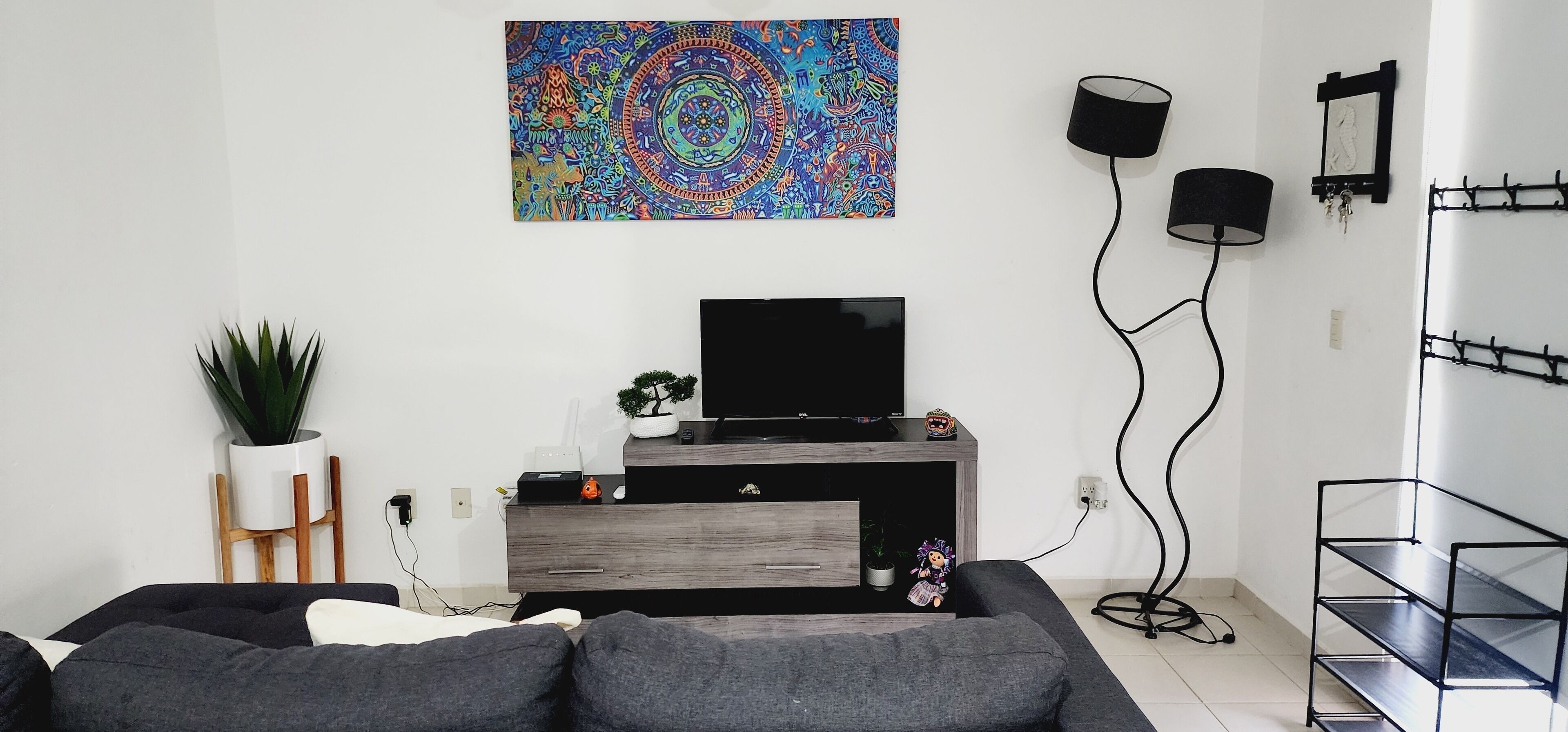 Un salon moderne avec un téléviseur à écran plat, une table basse, un canapé, une étagère murale, une plante en pot et un tableau abstrait aux couleurs vives.