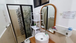 A bathroom with a white sink, a mirror, and a toilet. There is a shelf with toiletries and a notice about not flushing trash. - Charming bungalow with AC and WiFi in peaceful Angeles (Angeles)