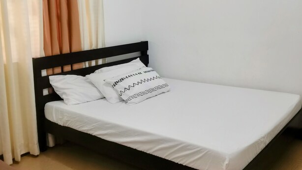 A single bed with white bedding and black headboard, a small table with a remote control, an air conditioning unit, a framed picture of flowers, and a wall-mounted light fixture. - Charming bungalow with AC and WiFi in peaceful Angeles (Angeles)