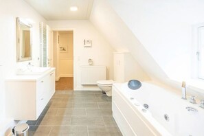 A modern bathroom with a large bathtub, a toilet, and a sink with a mirror. - Semi-detached House Waygaard West, Dagebull (Dagebuell)