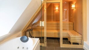 Un sauna avec des bancs en bois et des portes en verre, une baignoire blanche et un plafond en pente.