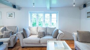 Un salon avec un ensemble de canapés beige, une table basse blanche et une grande fenêtre donnant sur un paysage verdoyant.