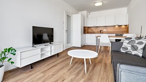 A modern living room with a flat-screen TV, a white sofa, a small round table, and a kitchen area with white cabinets and a wooden countertop. - Plešivec by Interhome (Abertamy)