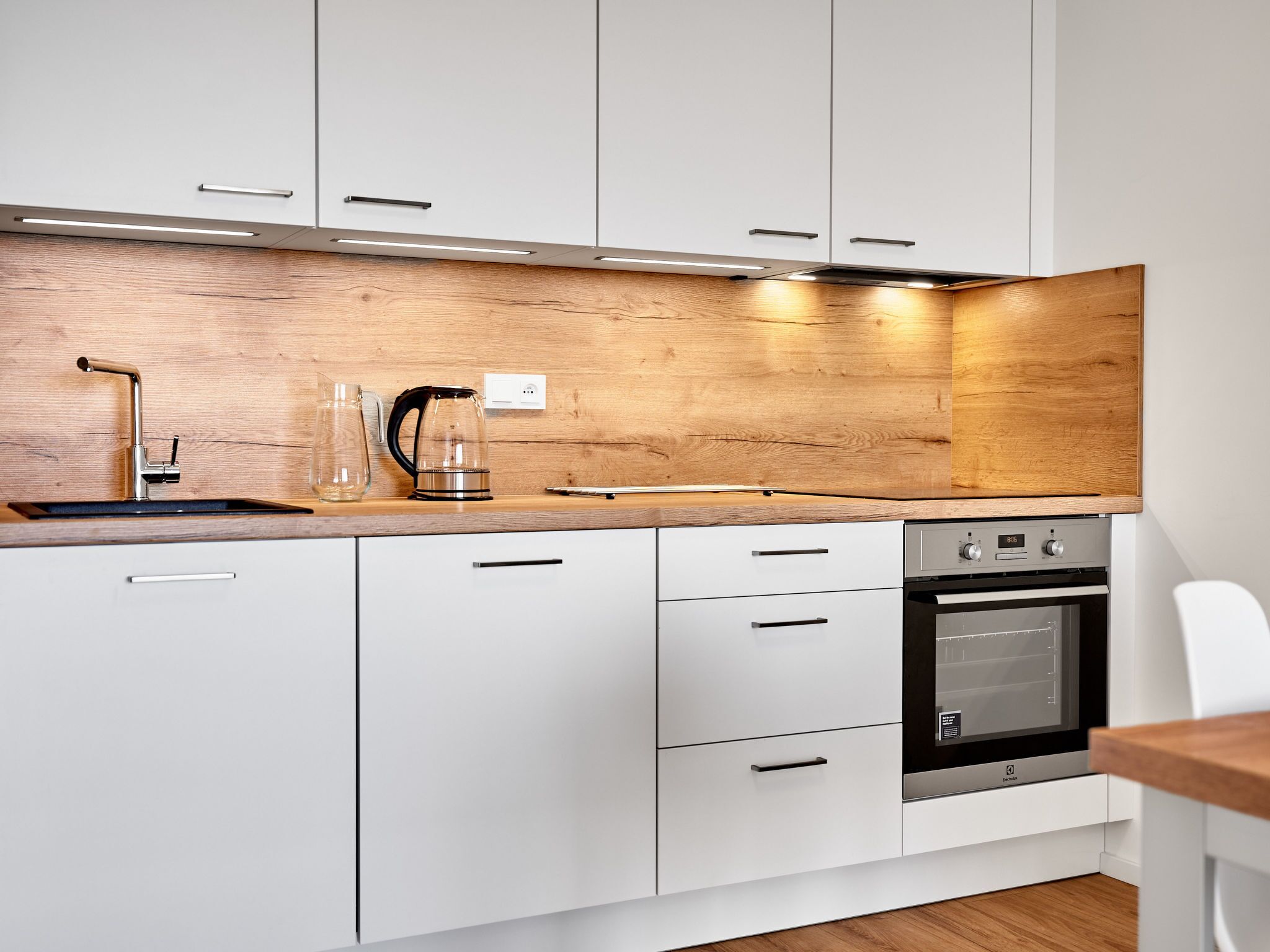 A modern kitchen with white cabinets, a wooden backsplash, stainless steel appliances, and a wooden countertop.