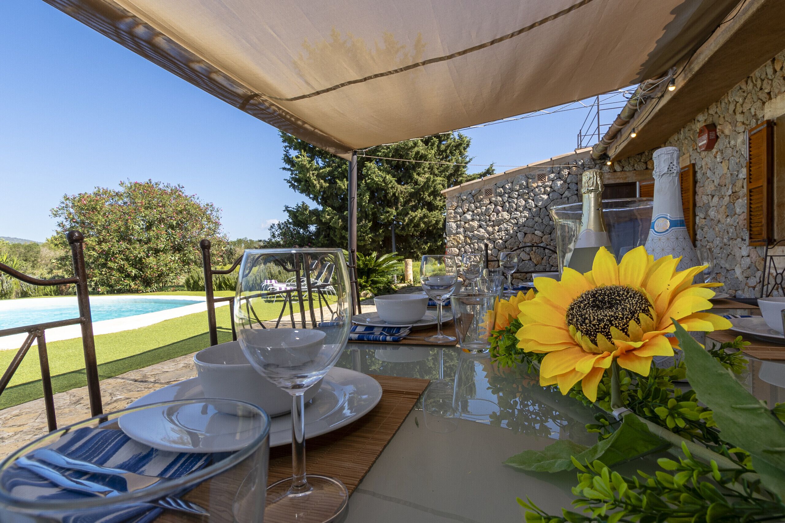 Une table à manger dressée pour six personnes, avec une vue dégagée sur une piscine et un mur de pierre en arrière-plan.