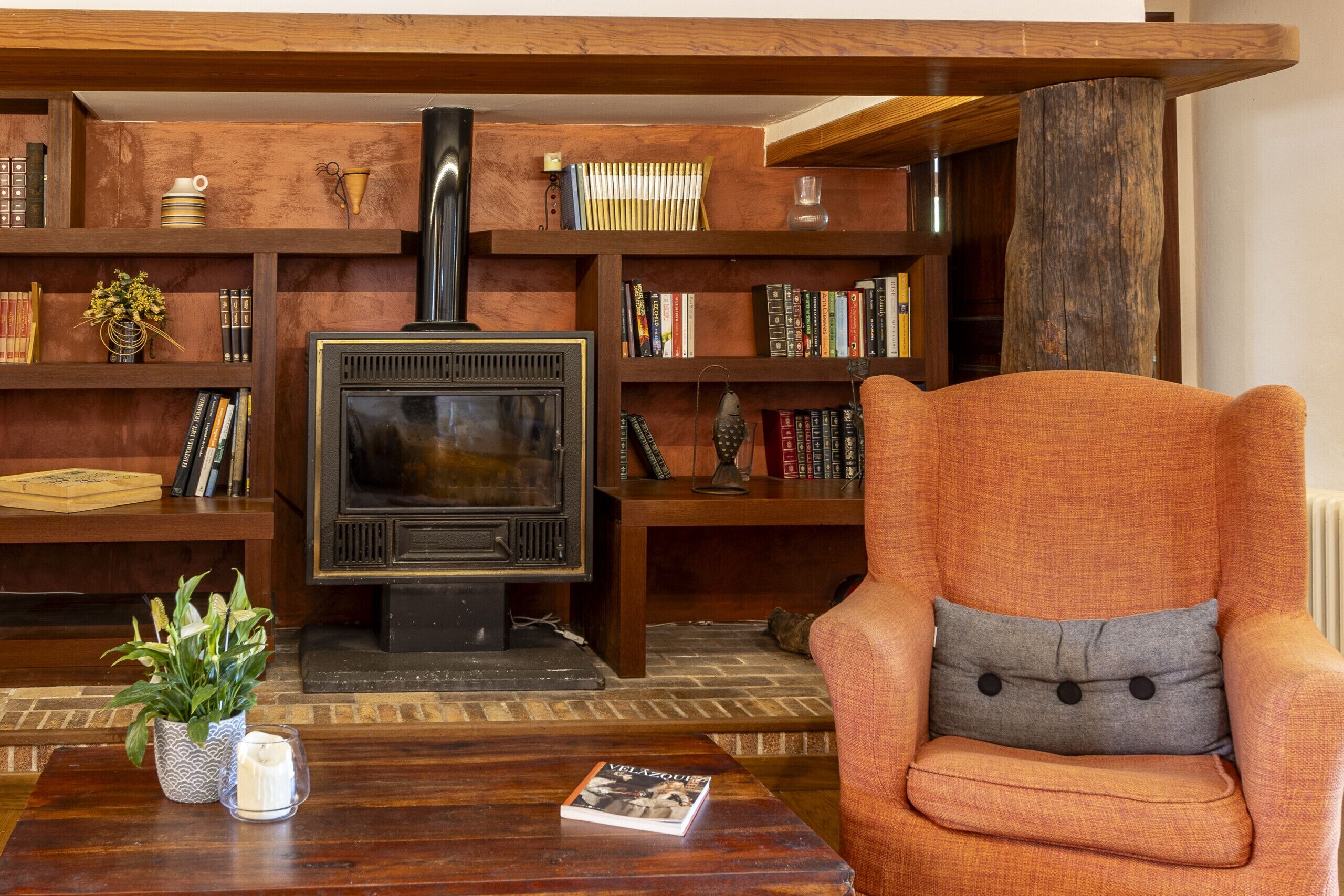A cozy living room with a fireplace, wooden bookshelves, and a comfortable armchair.
