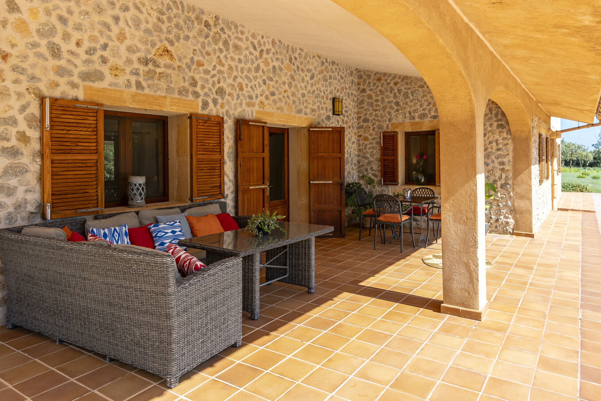A covered outdoor seating area with a stone wall, wicker furniture, and a tiled floor.