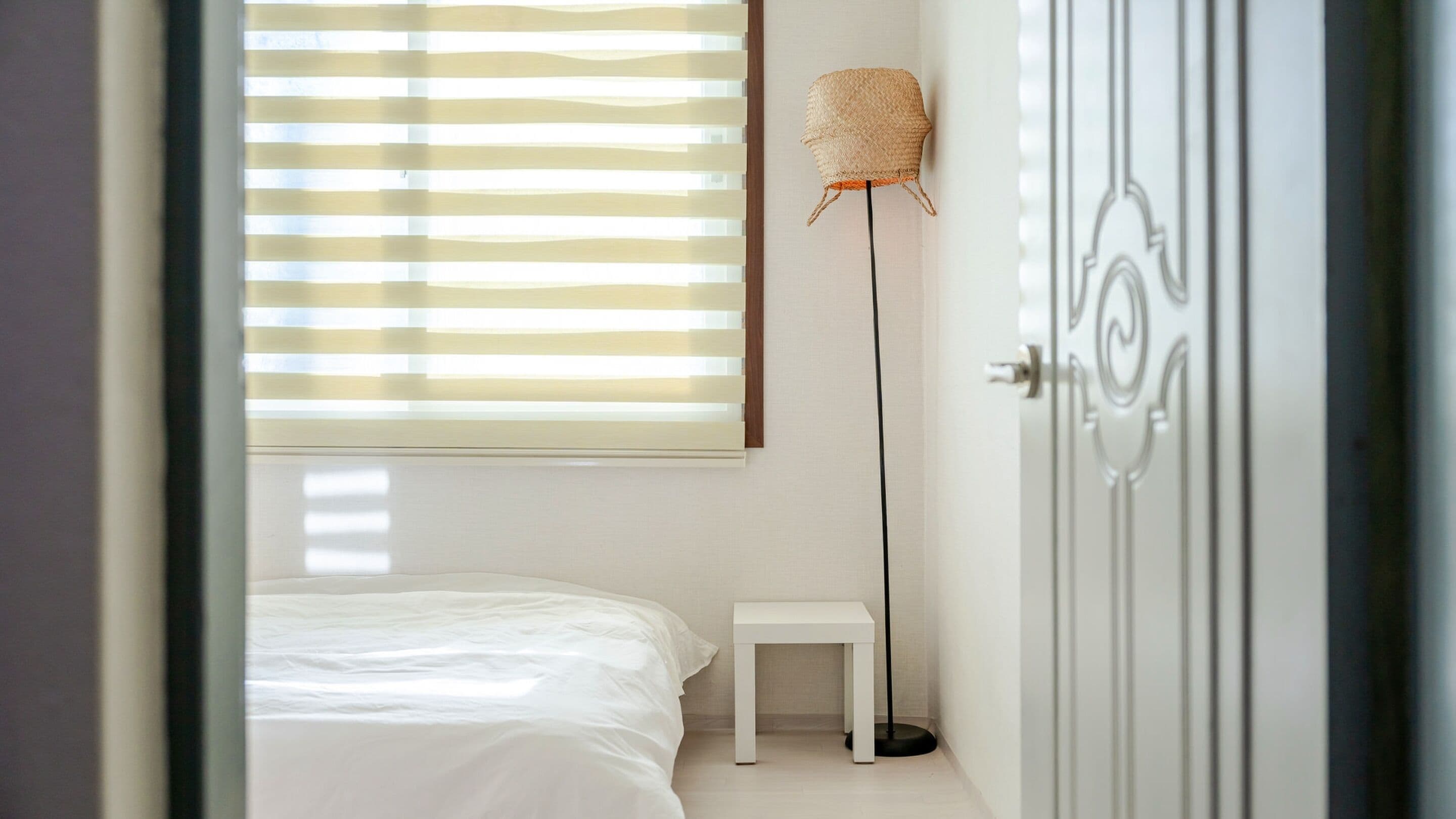 A bedroom with a bed, a small bedside table, a floor lamp, and a door.