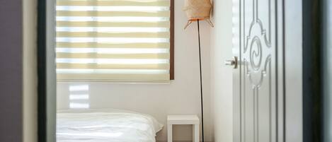 A bedroom with a bed, a small bedside table, a floor lamp, and a door.