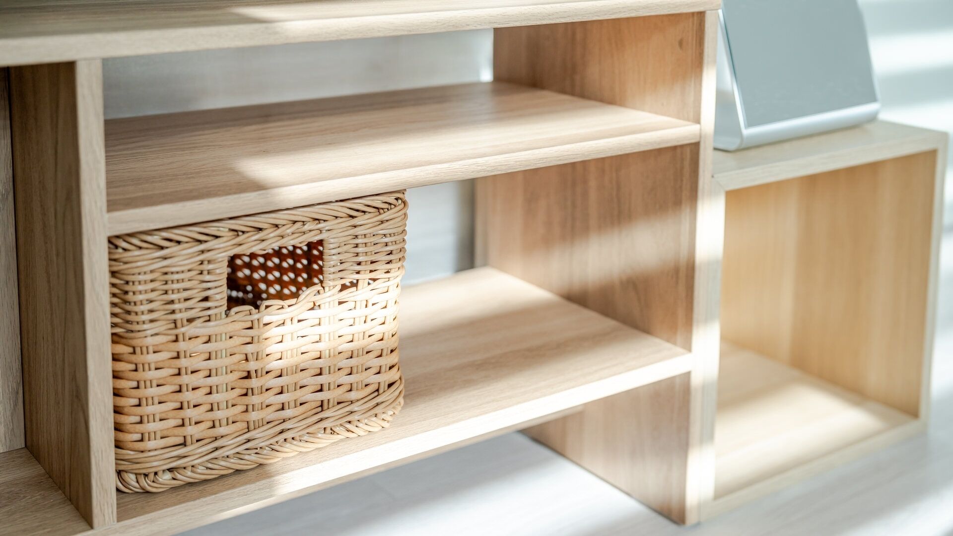 A wooden shelf unit with a woven basket on the left shelf.