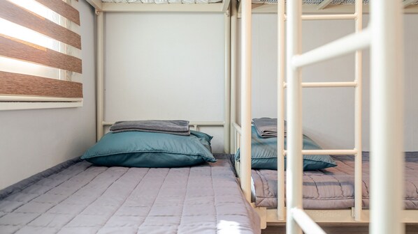 A bunk bed with a grey quilt and teal pillows, a window with wooden blinds, and a white wall. - Gangneung Funny Group Pension (Gangneung)