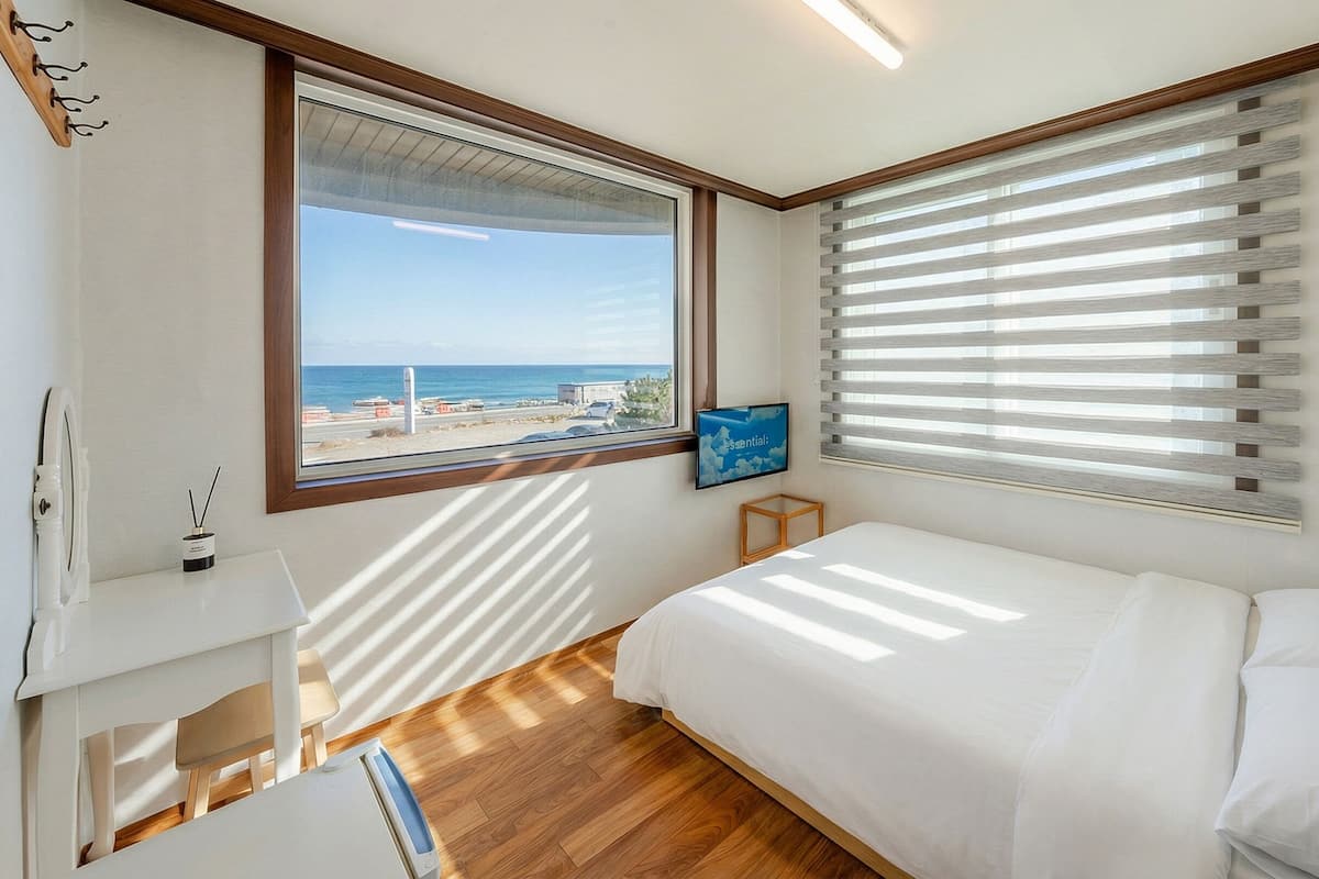 Un dormitorio con cama, mesita de noche, televisor y ventana con persianas.