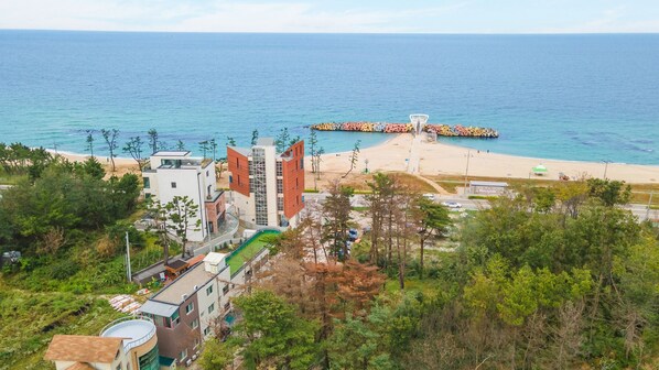 A coastal resort with modern buildings, a beach, and a sea wall with a basketball hoop. - Gangneung Funny Group Pension (Gangneung)