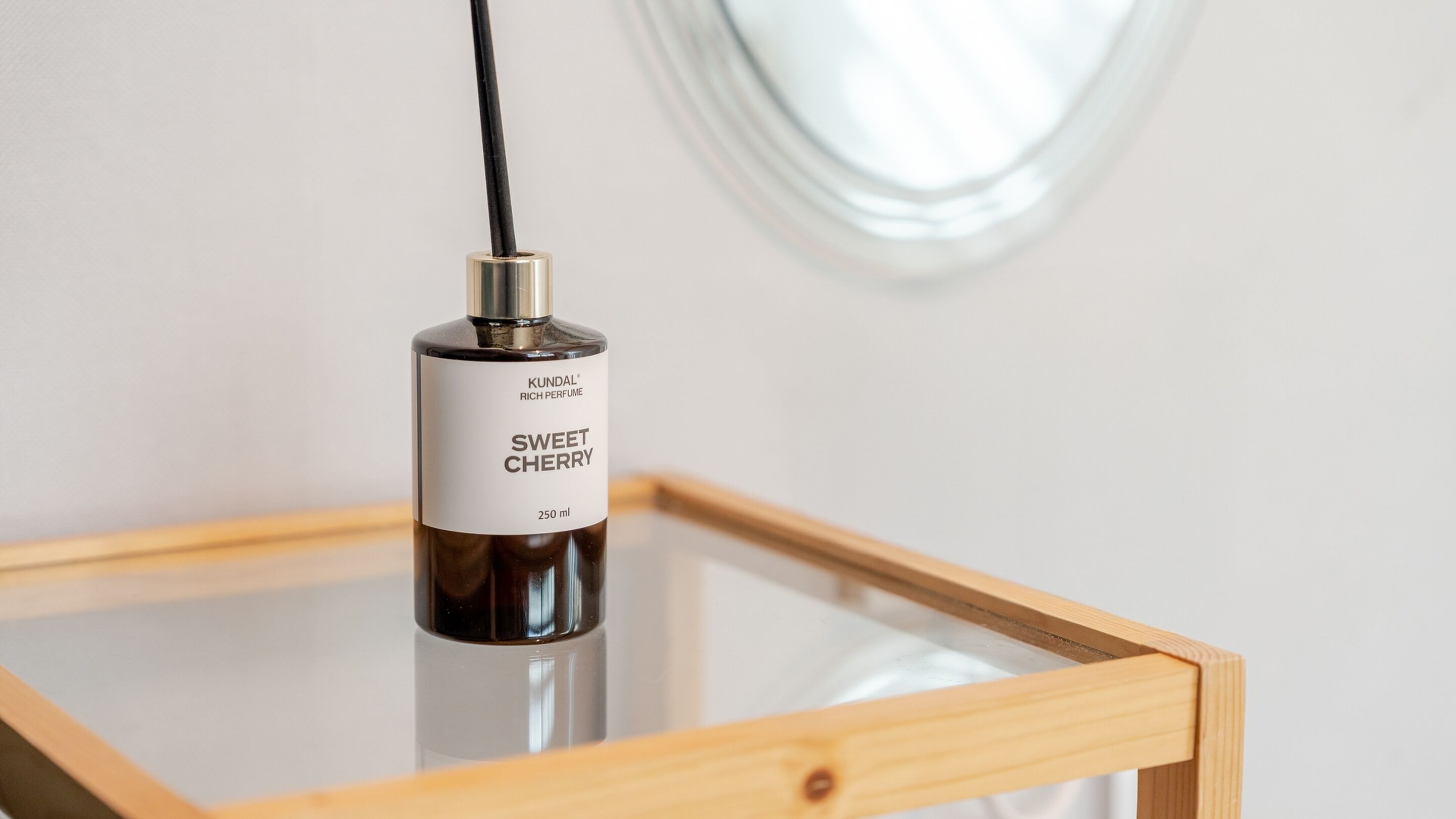 A bottle of KUNDAL® Sweet Cherry perfume on a glass table.