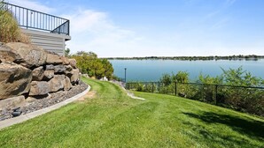 Una propiedad junto al lago con un muro de piedra, césped y una barandilla metálica con vistas al agua.