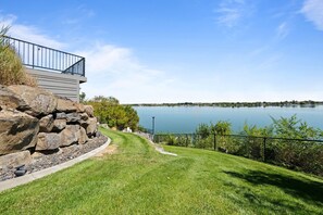 A lakeside property with a stone retaining wall, a grassy lawn, and a metal railing overlooking the water.