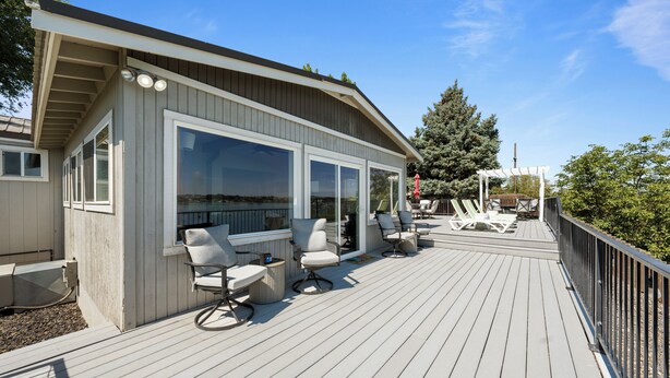 Una terraza de madera con mobiliario exterior, una pérgola y vistas del paisaje circundante.