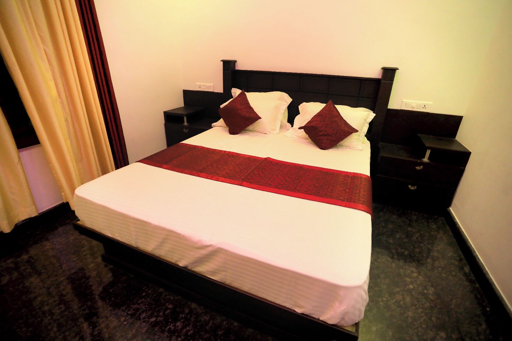 A neatly made bed with a white and red bedspread, two dark red pillows, and a black headboard.