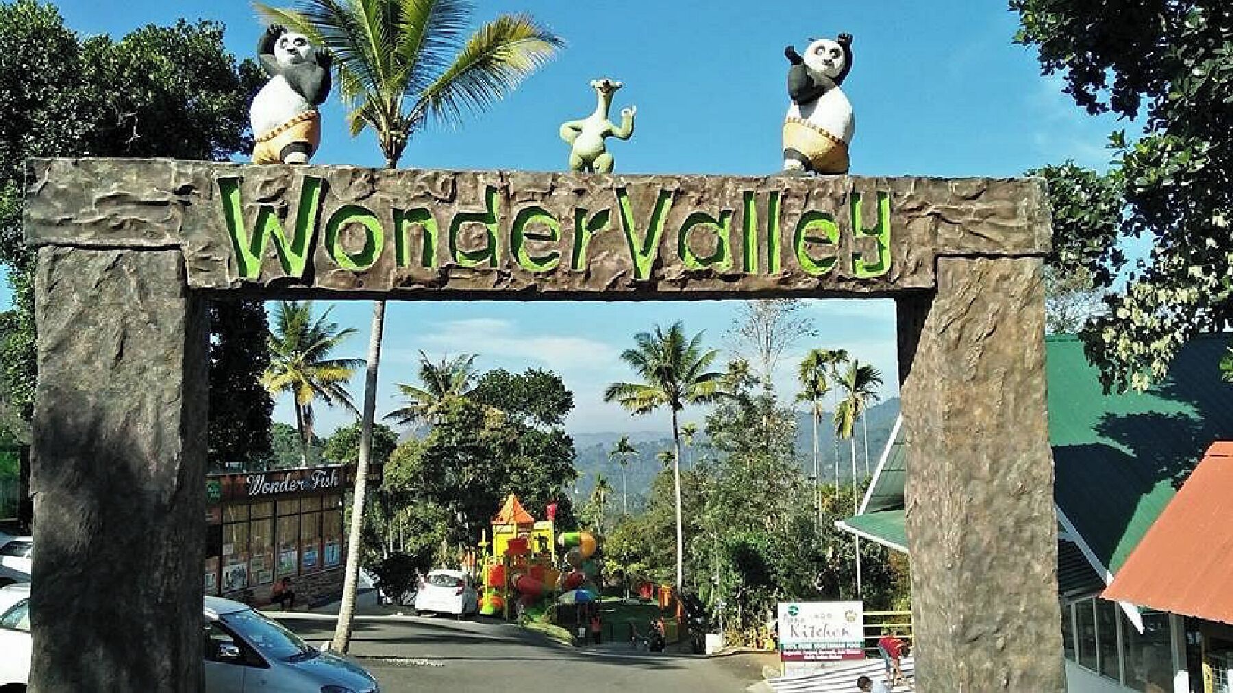 A sign with 'Wonder Valley' written on it, surrounded by palm trees and a view of a colorful building in the background.