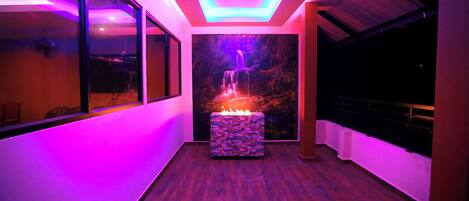 A modern interior with a stone fireplace, a waterfall mural, and vibrant LED lighting.