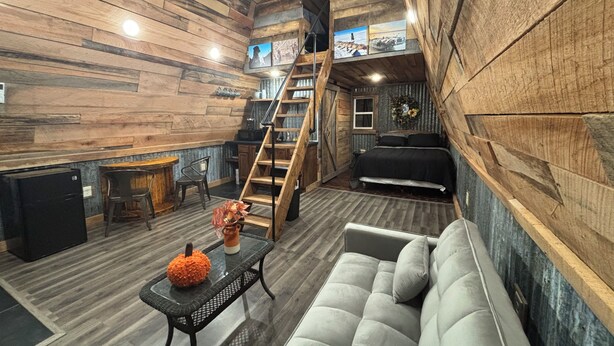 A loft-style room with a wooden interior, a sofa, a table with a pumpkin decoration, and a staircase leading to an upper level. - Peaceful secluded cabin located near Horseshoe Lake  (Miller City)