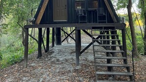 A wooden cabin with a triangular roof, a front door, and a small porch with chairs. - Peaceful secluded cabin located near Horseshoe Lake  (Miller City)