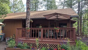 A wooden cabin with a covered porch, outdoor seating, and a garden area with various plants and flowers. - Garden Cabin with Fenced Yard and AC (Pinetop)