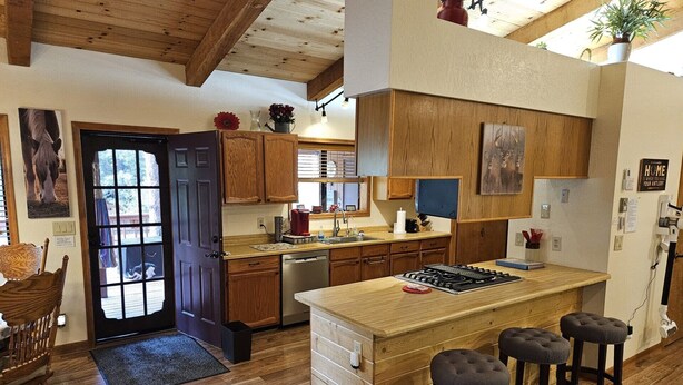 A kitchen with wooden cabinets, a central island with stools, a dishwasher, and a stove. - Garden Cabin with Fenced Yard and AC (Pinetop)