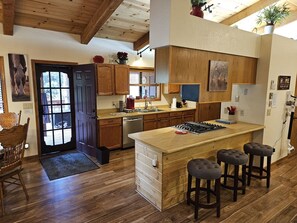 A kitchen with wooden cabinets, a central island with stools, a dishwasher, and a stove. - Garden Cabin with Fenced Yard and AC (Pinetop)
