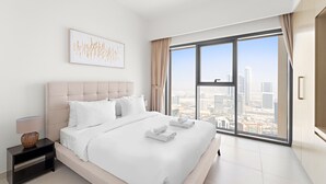 A modern bedroom with a large bed, a nightstand, a lamp, and a city view through large windows.
