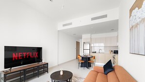 A modern living room with a large flat-screen TV, a sofa, a coffee table, and a dining area with a table and chairs.