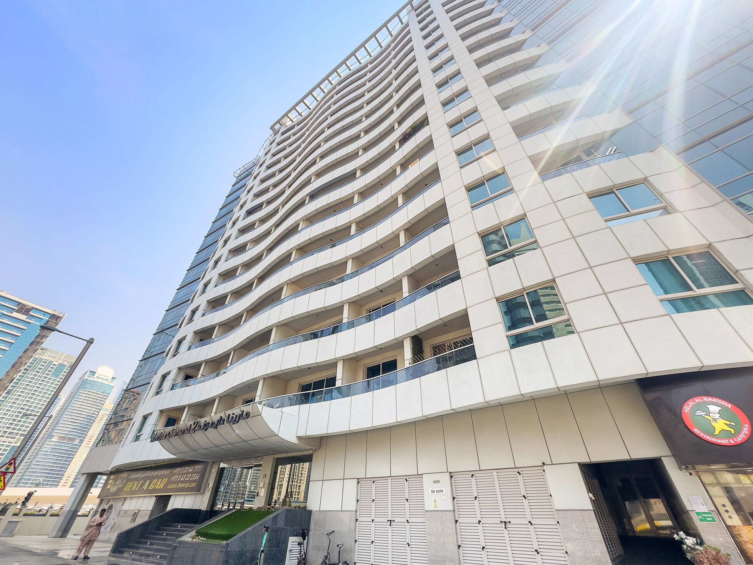 A modern high-rise building with multiple balconies and a restaurant on the ground floor.