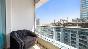 Un balcón con vistas a un paisaje urbano, un sofá marrón oscuro y una barandilla de cristal.