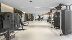Un gimnasio con varias máquinas de ejercicio, una pared con vegetación y un techo con iluminación empotrada.