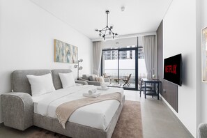 A modern hotel room with a large bed, a TV, a balcony with a view, and a dining area. - Modern Studio with Great Amenities (Dubai)