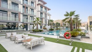 Un edificio moderno con piscina, mobiliario exterior y palmeras.
