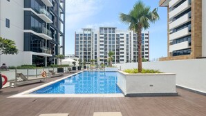 A modern apartment complex with a central swimming pool, lounge areas, and a palm tree. - Modern Studio in Prime Meydan Area (Dubai)