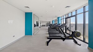 A gym with treadmills aligned along a wall with large windows. - Modern Studio in Prime Meydan Area (Dubai)