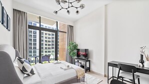A modern hotel room with a large bed, a desk, a TV, and a balcony with a city view. - Modern Studio in Prime Meydan Area (Dubai)