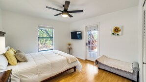 Un dormitorio con cama, una banca, ventilador de techo, televisor y ventana.