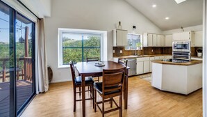 Una cocina amplia con una isla grande, mesa de comedor de madera y sillas. Se ve vegetación a través de la ventana.