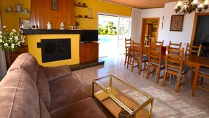 A living room with a brown sofa, a glass coffee table, wooden dining table with chairs, a kitchen area with yellow walls, and a fireplace. - Villa Petit Castell 10 people Costa Brava (PALAFOLLS)