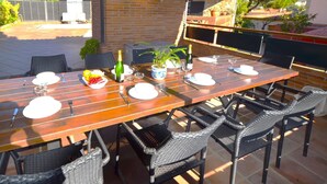 An outdoor patio with a wooden table set for dining, surrounded by wicker chairs. - Villa Petit Castell 10 people Costa Brava (PALAFOLLS)