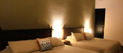 Habitación de hotel con dos camas, cada una con cabecera y mesitas de noche.