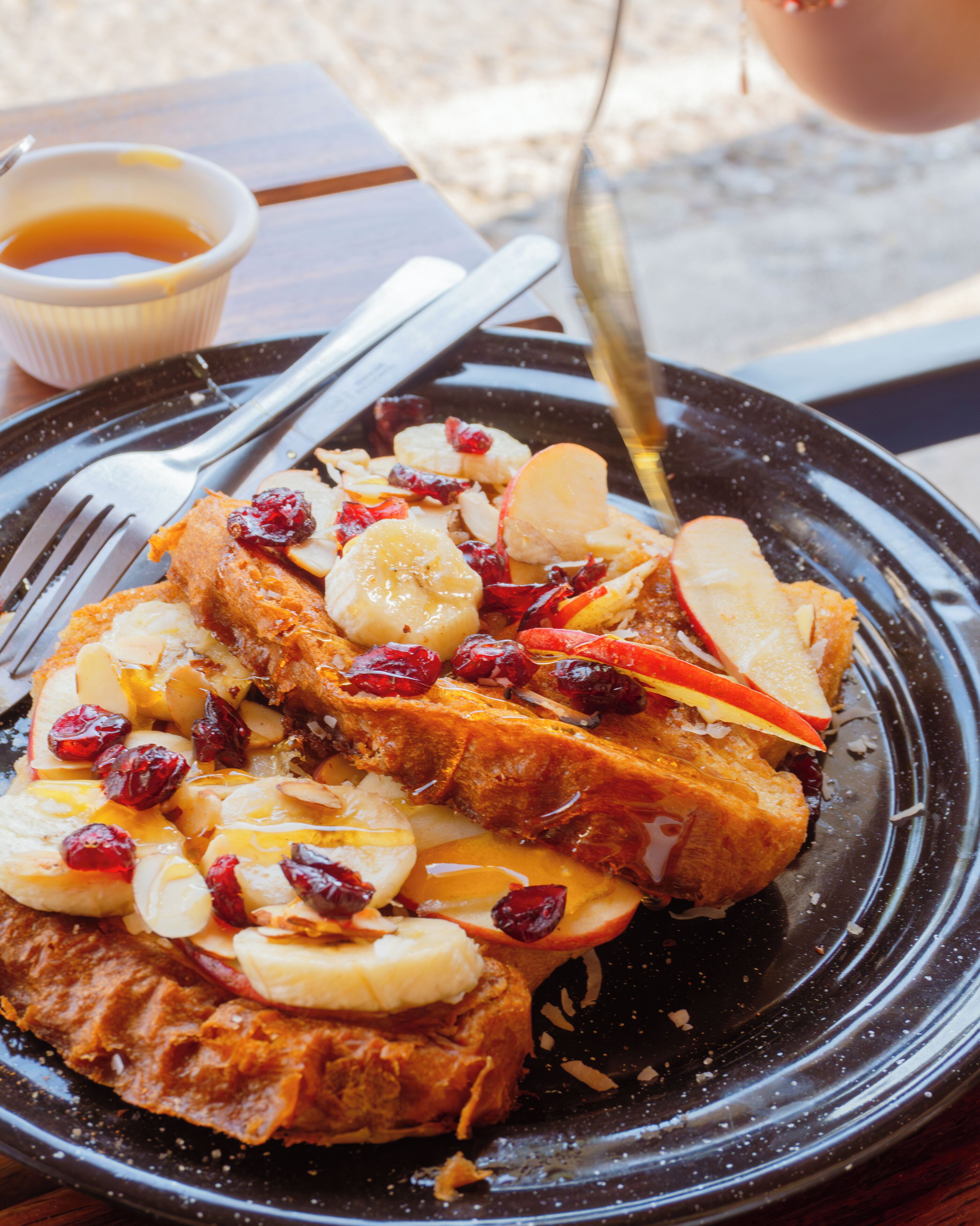 A plate of French toast with apples and cranberries, a fork, and a small bowl of syrup.